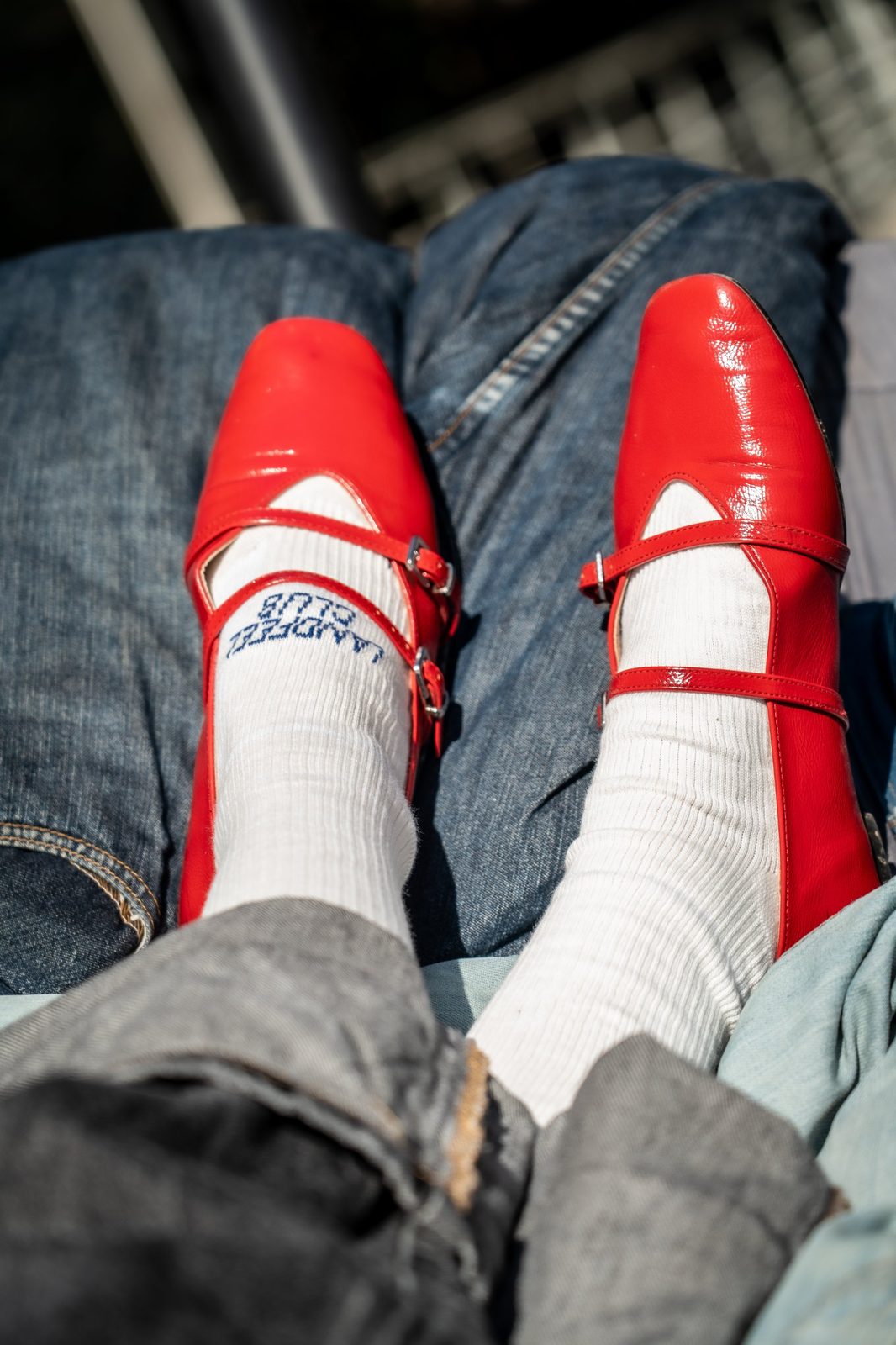 Two feet in cream Landfeel Club socks and red shoes, resting on denim